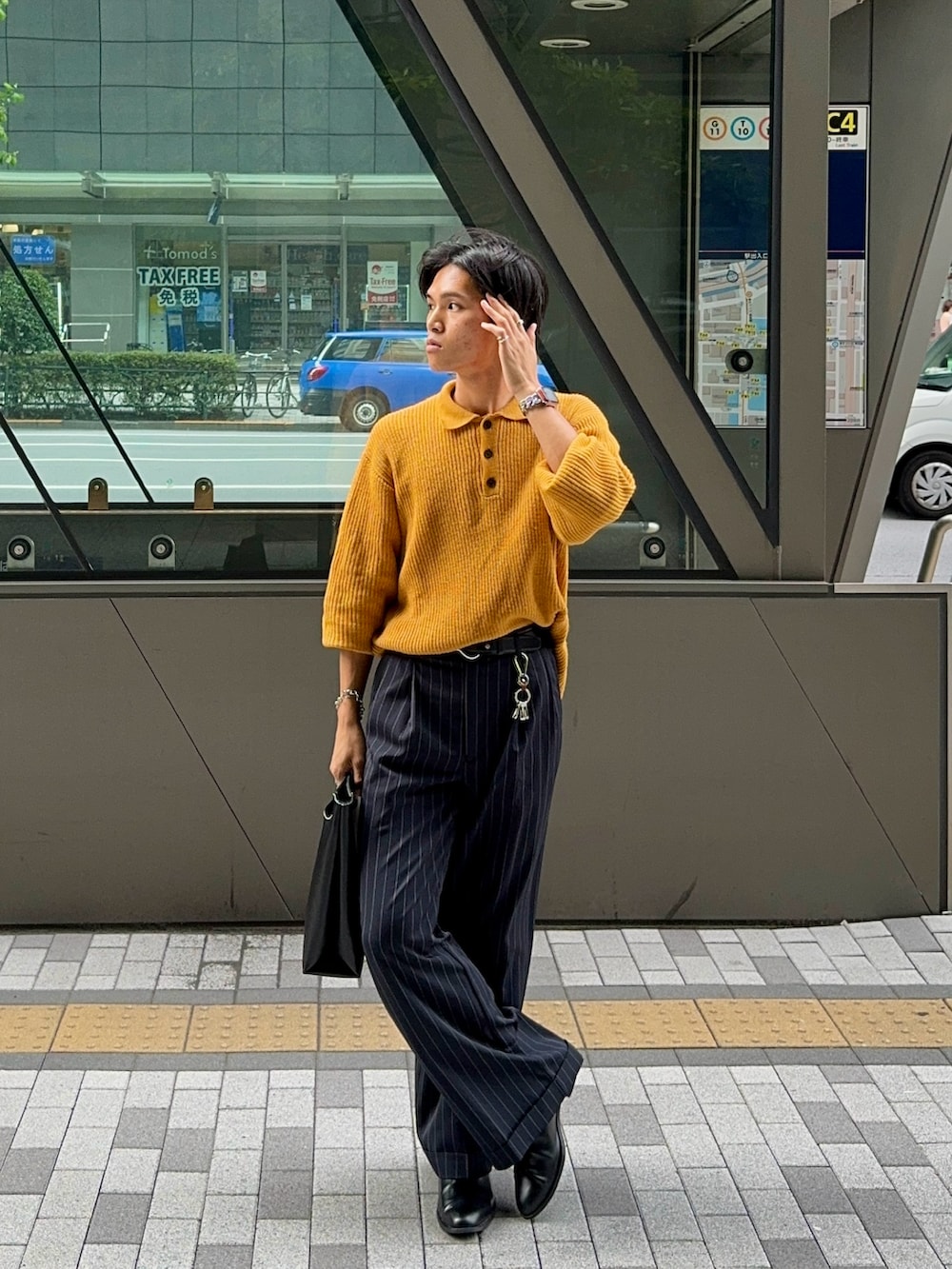 ブラック系のスラックス、イエロー系のニット/セーター、ブラック系のハンドバッグを着用したメンズの夏コーディネートの5枚目の写真
