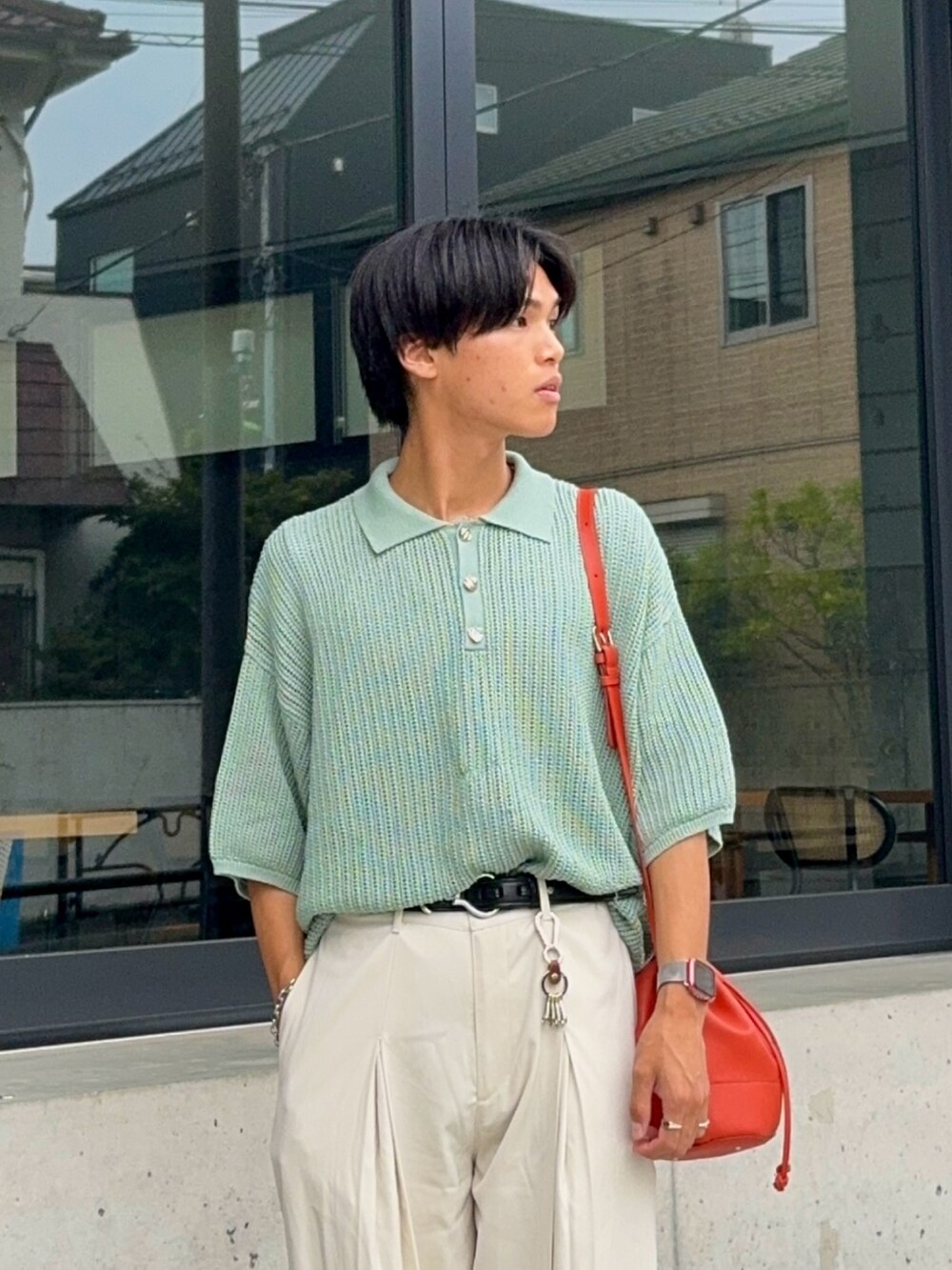 グリーン系のポロシャツ、オレンジ系のバッグ、ホワイト系のスラックスを着用したメンズの夏コーディネートの3枚目の写真