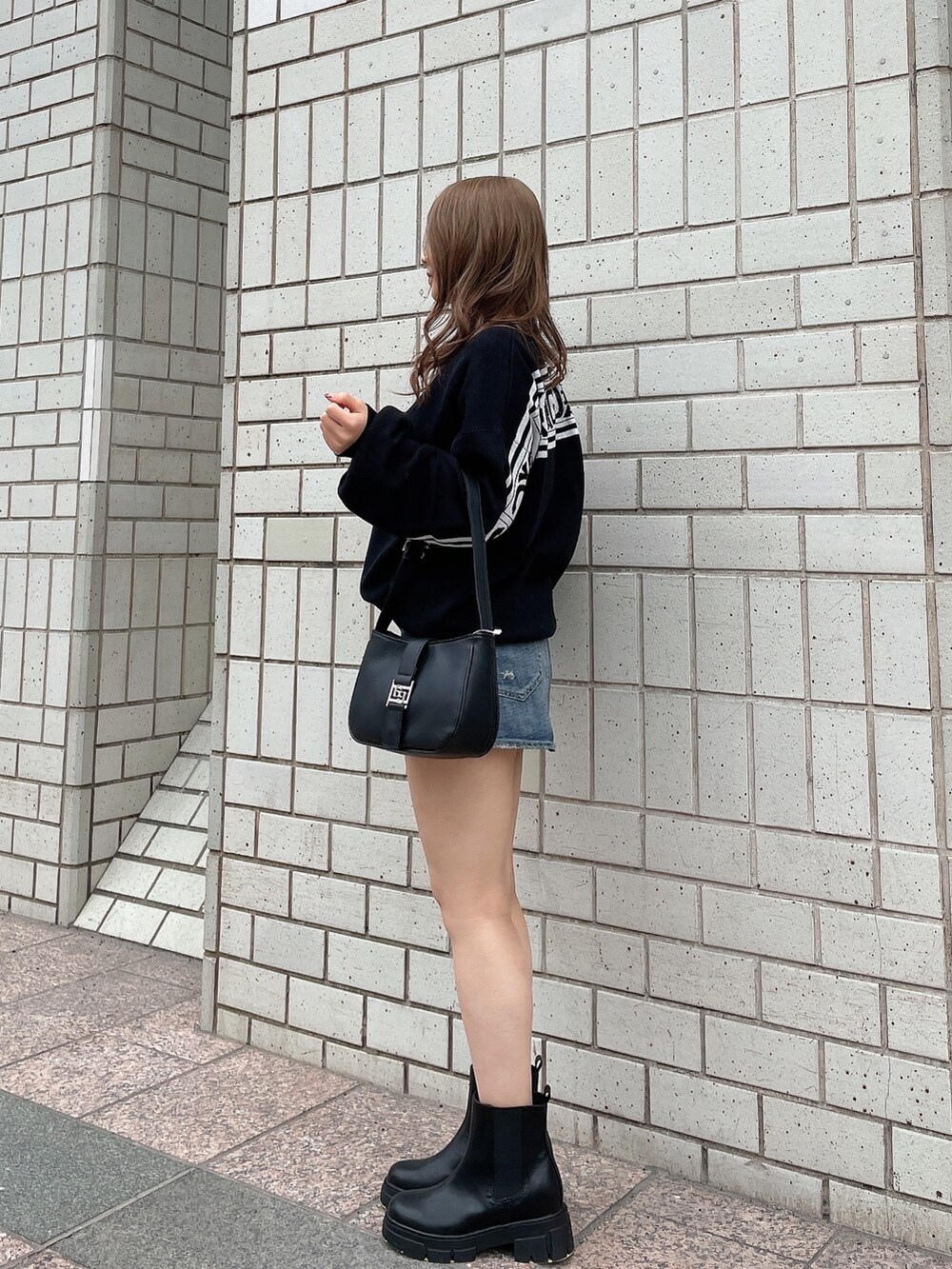 ブラック系のニット/セーター、ブルー系のデニムスカート、ブラック系のハンドバッグを着用したレディースの冬コーディネートの2枚目の写真