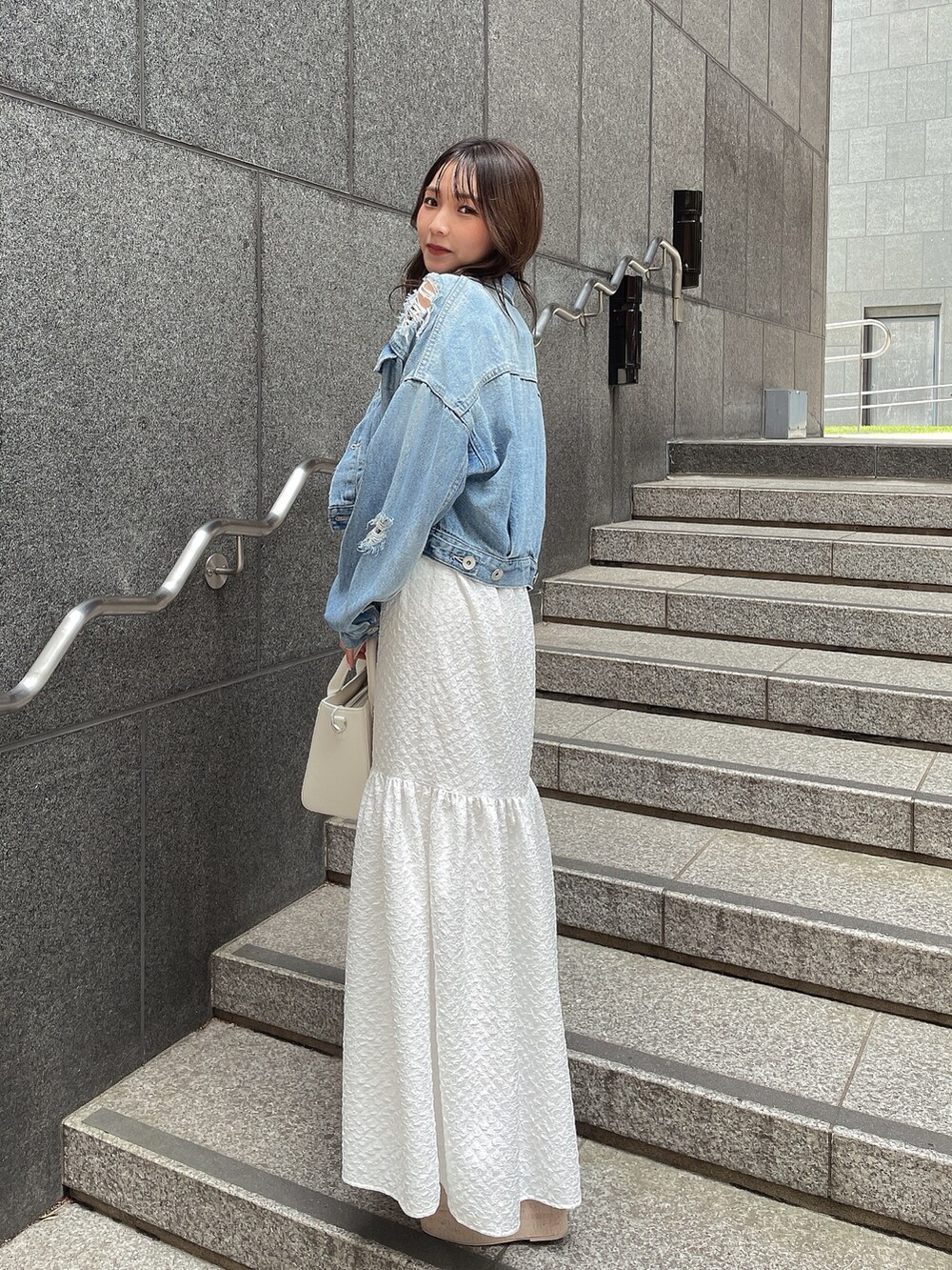 ブルー系のデニムジャケット、ホワイト系のサンダル、ホワイト系のハンドバッグを着用したレディースの春コーディネートの2枚目の写真