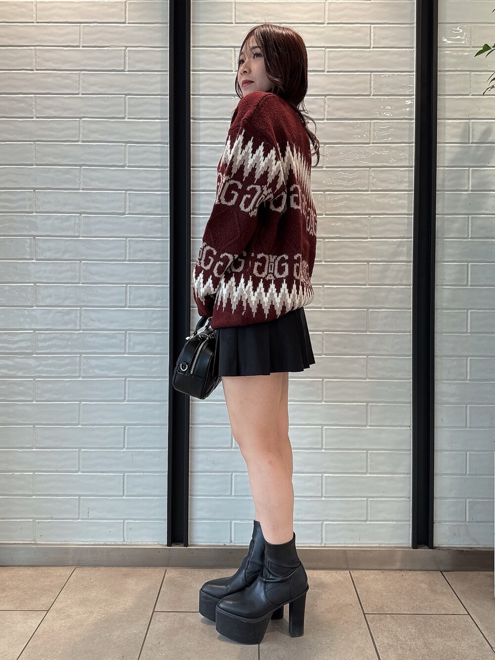レッド系のニット/セーター、ブラック系のスカート、ブラック系のハンドバッグを着用したレディースの冬コーディネートの2枚目の写真