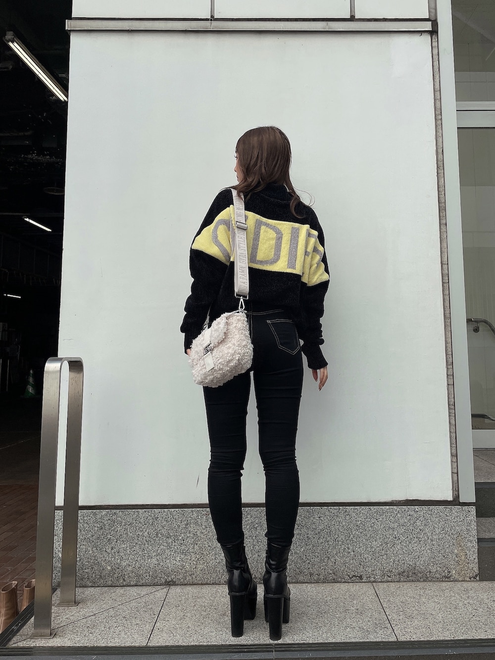 ブラック系のニット/セーター、ホワイト系のハンドバッグ、ブラック系のデニムパンツを着用したレディースの秋コーディネートの4枚目の写真