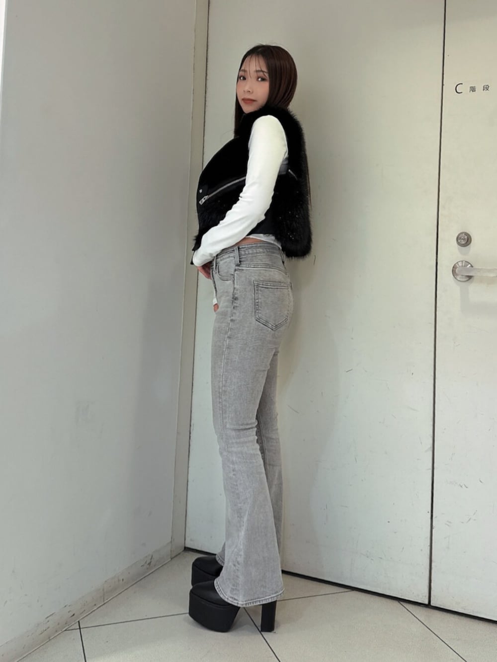 グレー系のデニムパンツ、ブラック系のブーツ、ブラック系のベストを着用したレディースの秋コーディネートの2枚目の写真