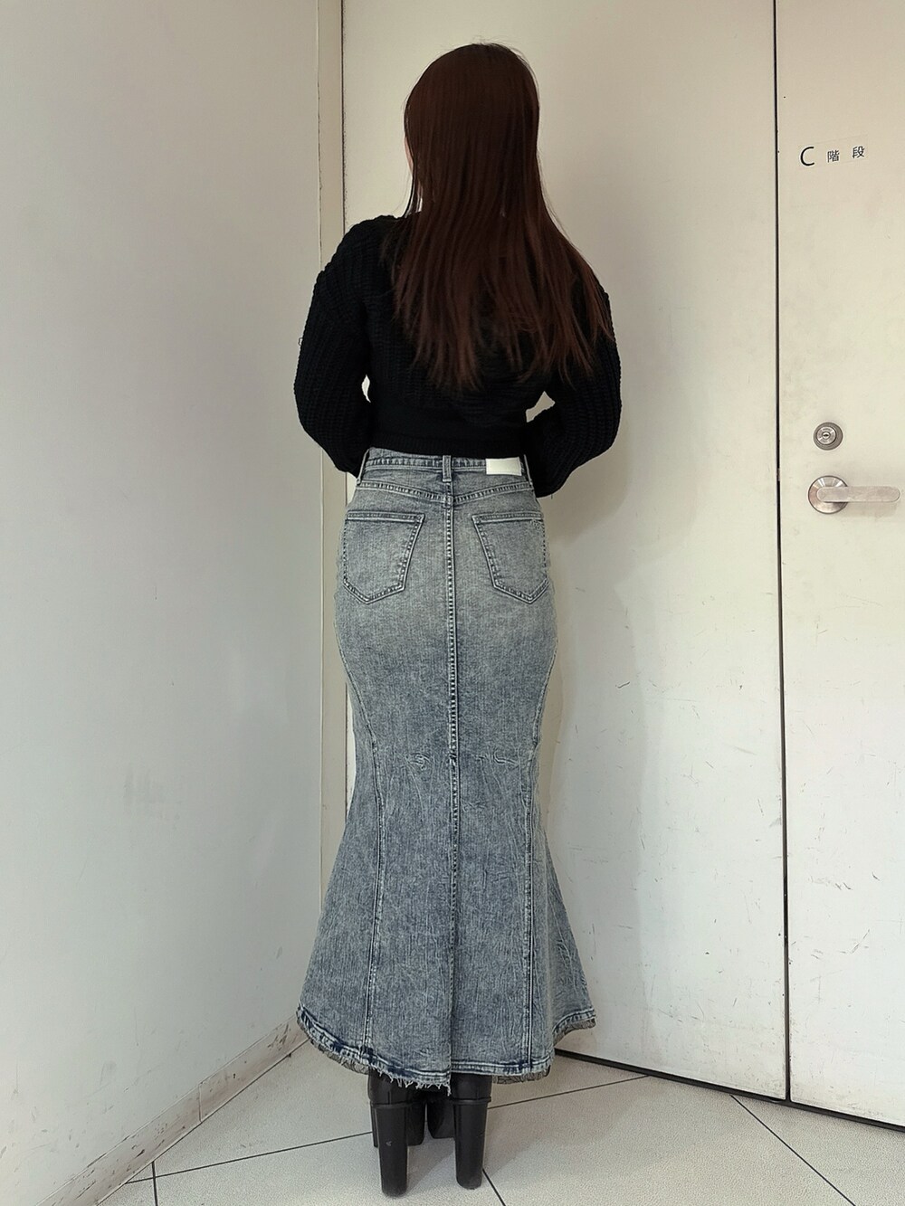 ブルー系のデニムスカート、ブラック系のニット/セーター、ブラック系のブーツを着用したレディースの冬コーディネートの3枚目の写真