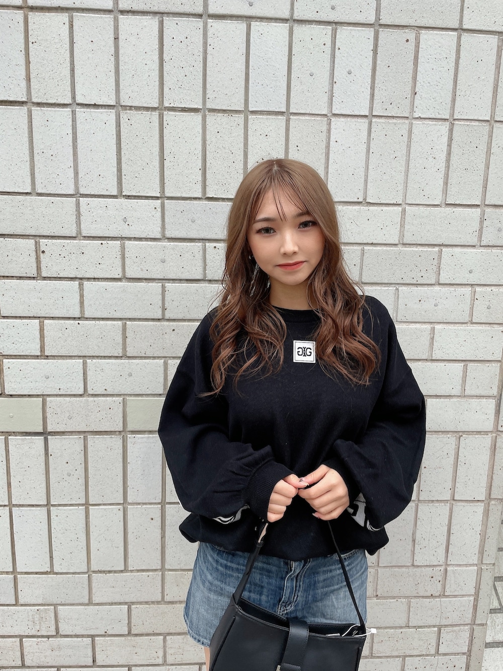 ブラック系のニット/セーター、ブルー系のデニムスカート、ブラック系のハンドバッグを着用したレディースの冬コーディネートの4枚目の写真