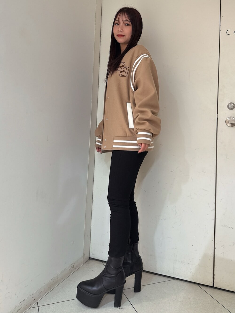 ブラック系のデニムパンツ、ブラック系のニット/セーター、ベージュ系のスタジャンを着用したレディースの秋コーディネートの2枚目の写真