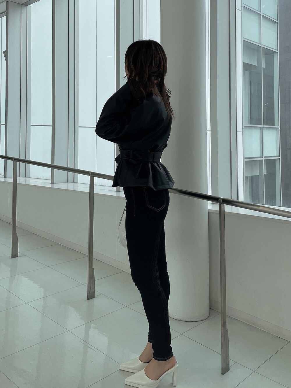 ブラック系のライダースジャケット、ブラック系のデニムパンツ、ホワイト系のハンドバッグを着用したレディースの冬コーディネートの2枚目の写真