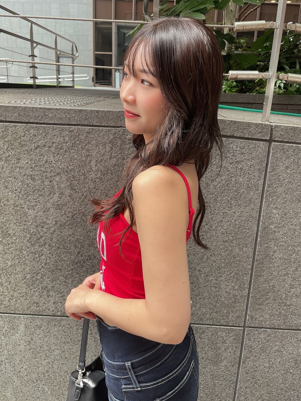 レッド系のキャミソール、ブルー系のデニムパンツ、ブラック系のショルダーバッグを着用したレディースの夏コーディネートの5枚目の写真