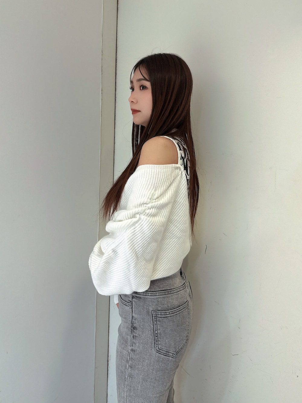 グレー系のデニムパンツ、ブラック系のブーツ、ホワイト系のニット/セーターを着用したレディースの秋コーディネートの5枚目の写真