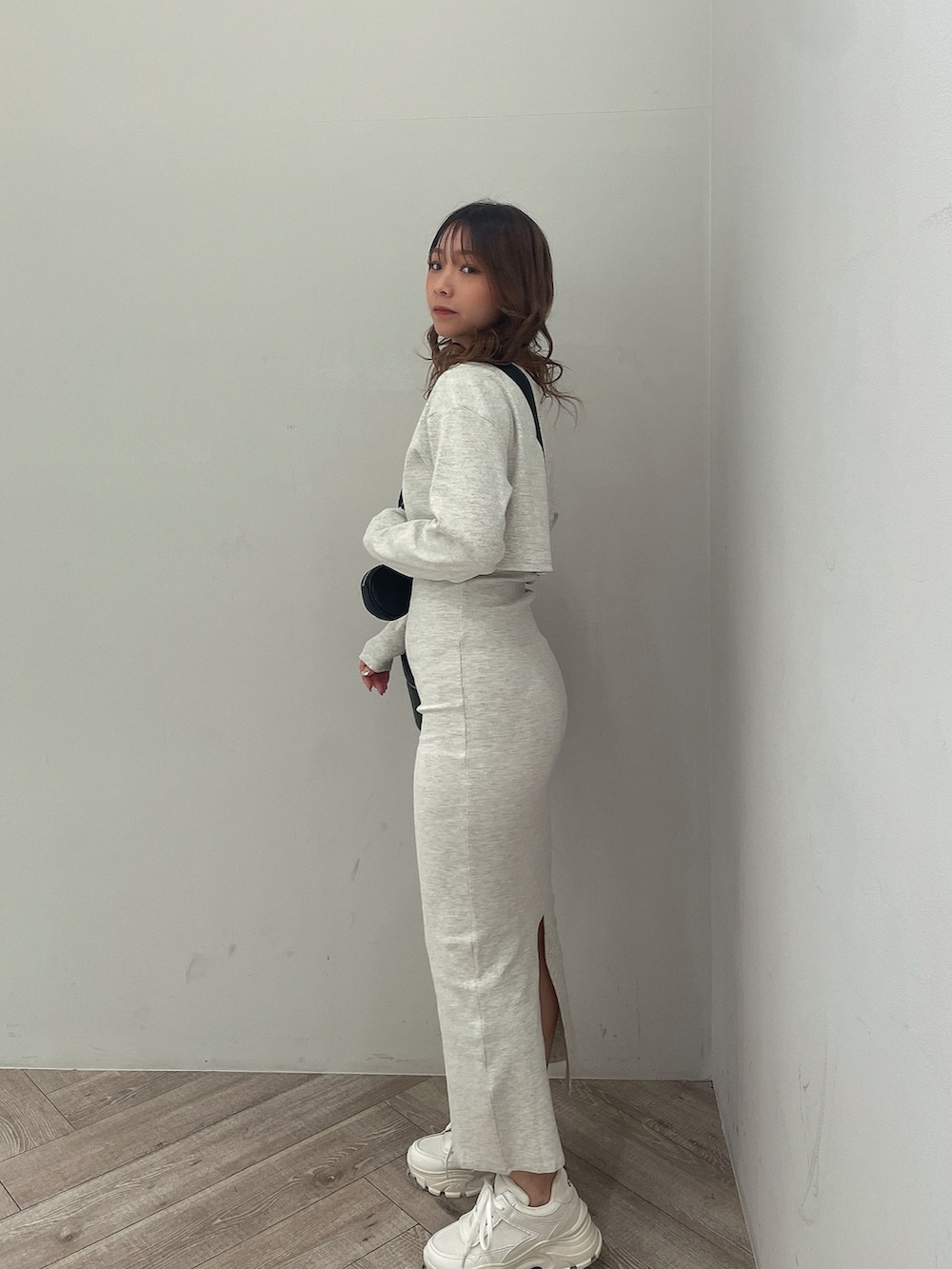 グレー系のワンピース、ブラック系のハンドバッグ、ホワイト系のスニーカーを着用したレディースの春コーディネートの2枚目の写真