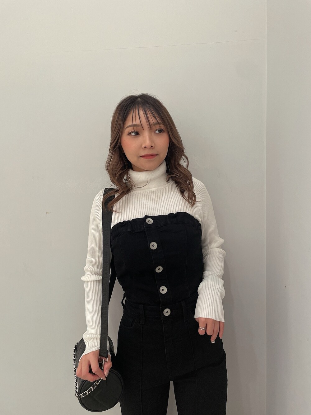 ホワイト系のニット/セーター、ブラック系のサロペット/オーバーオール、ブラック系のハンドバッグを着用したレディースの冬コーディネートの4枚目の写真