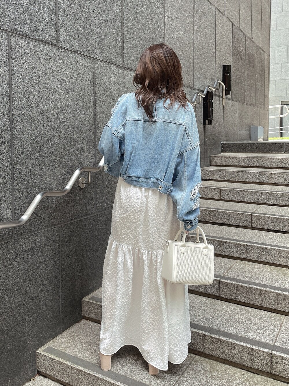 ブルー系のデニムジャケット、ホワイト系のサンダル、ホワイト系のハンドバッグを着用したレディースの春コーディネートの3枚目の写真