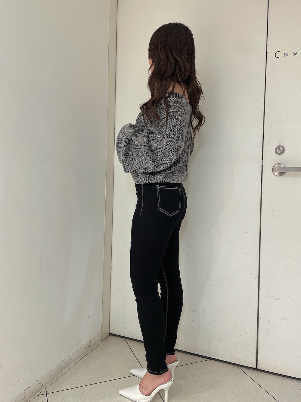 グレー系のニット/セーター、ブラック系のデニムパンツ、ホワイト系のパンプスを着用したレディースの夏コーディネートの2枚目の写真
