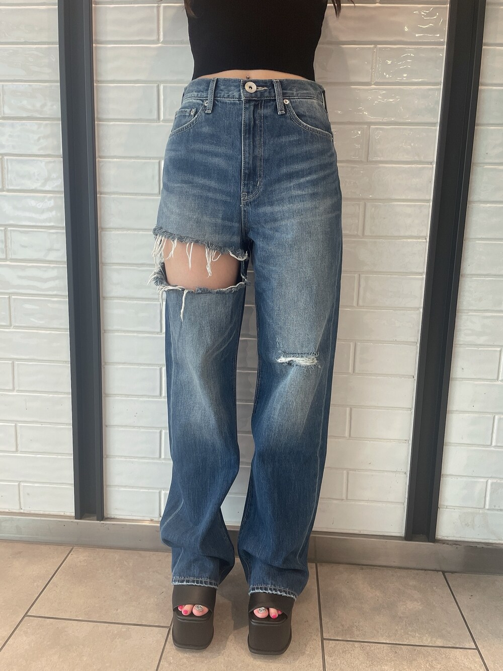 ブラック系のニット/セーター、ブラック系のサンダル、ブルー系のデニムパンツを着用したレディースの夏コーディネートの7枚目の写真