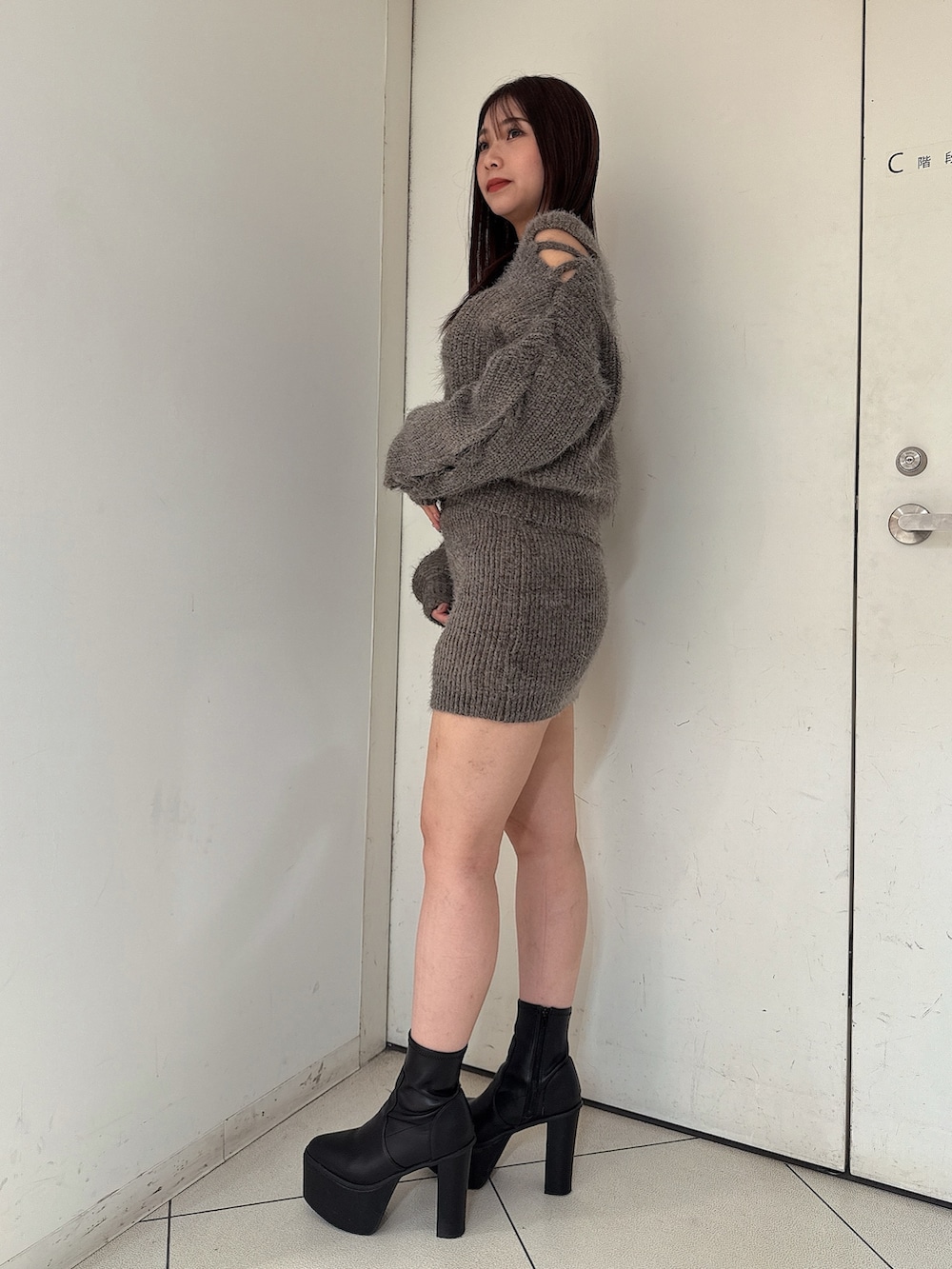 グレー系のニット/セーター、グレー系のスカート、ブラック系のブーツを着用したレディースの秋コーディネートの2枚目の写真