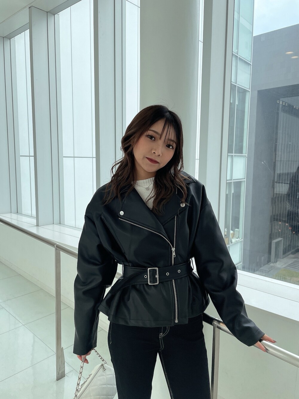 ブラック系のライダースジャケット、ブラック系のデニムパンツ、ホワイト系のハンドバッグを着用したレディースの冬コーディネートの3枚目の写真