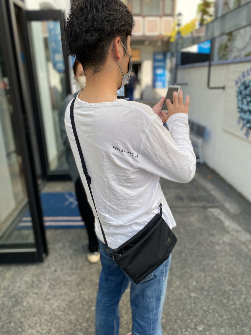 ホワイト系のトップス、ブルー系のデニムパンツ、ブラック系のショルダーバッグを着用したメンズの秋コーディネートの3枚目の写真