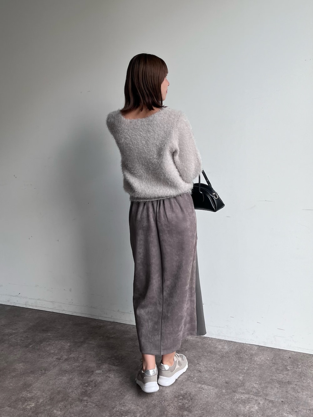 グレー系のニット/セーター、グレー系のスカート、ブラック系のトートバッグを着用したレディースの秋コーディネートの2枚目の写真