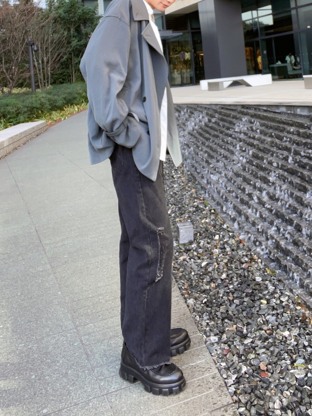 グレー系のトレンチコート、ブラック系のローファー、ホワイト系のその他を着用したメンズの冬コーディネートの2枚目の写真