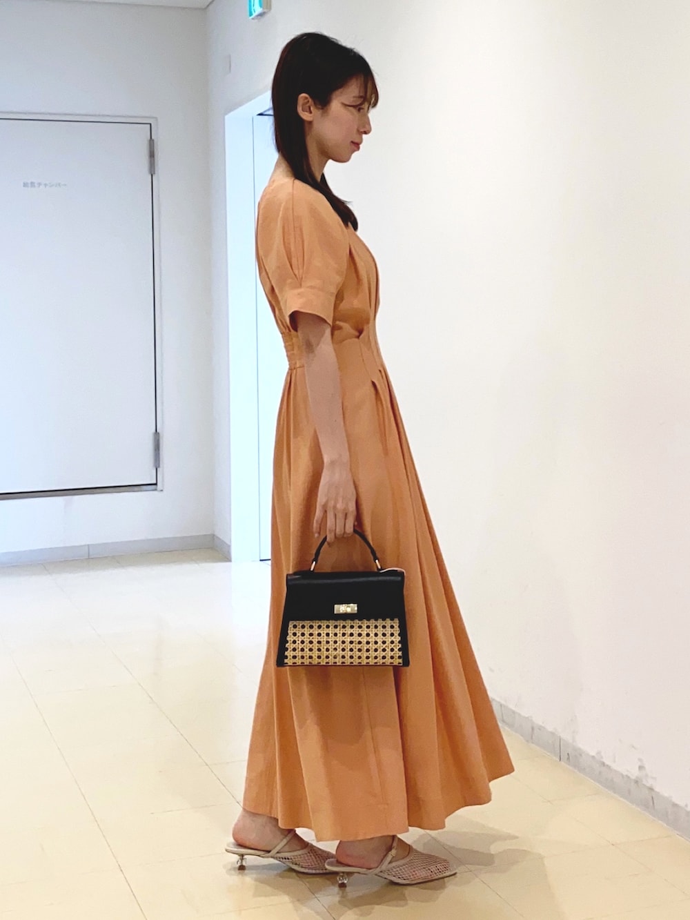 オレンジ系のワンピース、ブラック系のハンドバッグ、ホワイト系のサンダルを着用したレディースの春コーディネートの2枚目の写真