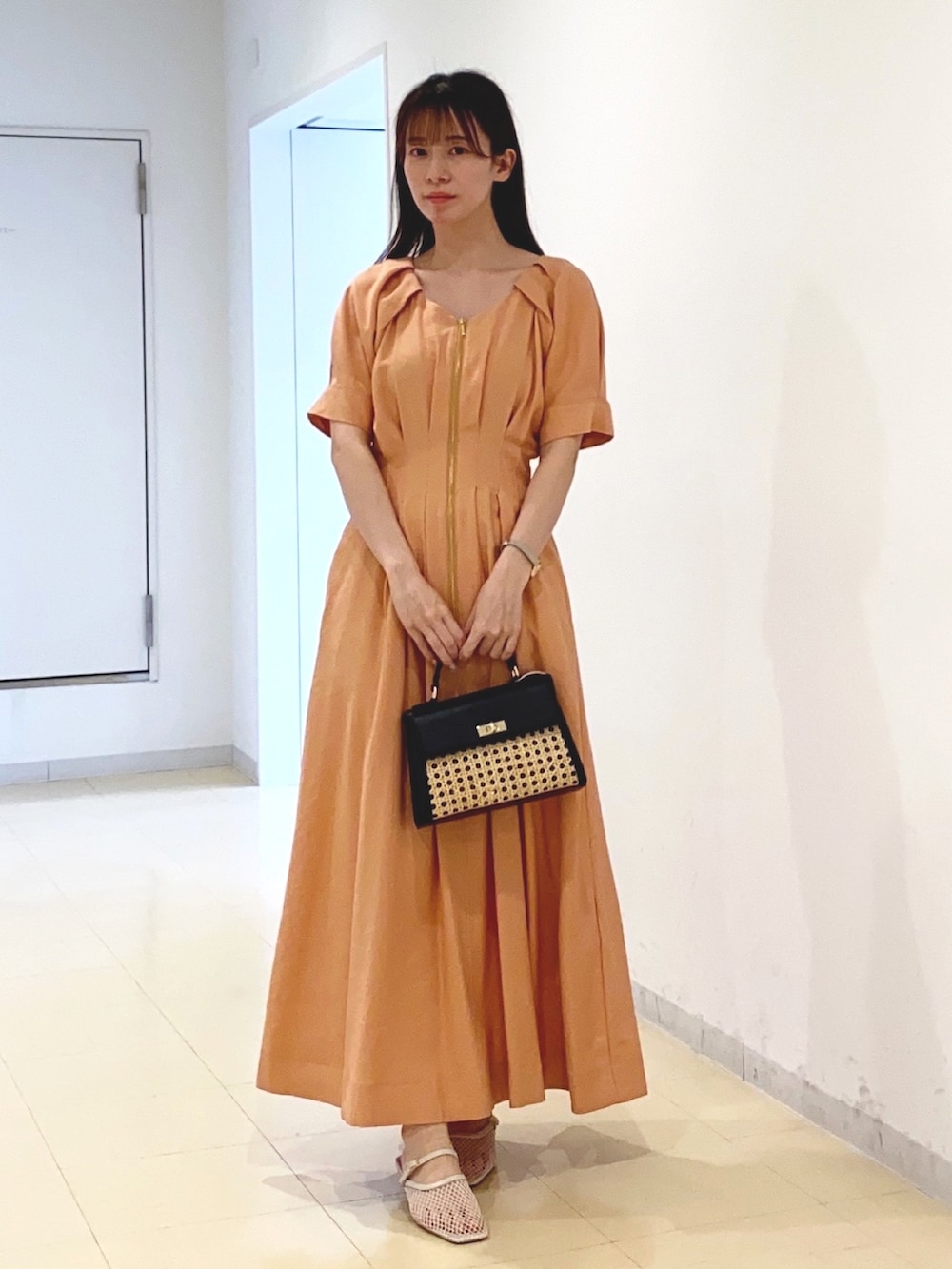 オレンジ系のワンピース、ブラック系のハンドバッグ、ホワイト系のサンダルを着用したレディースの春コーディネートの4枚目の写真