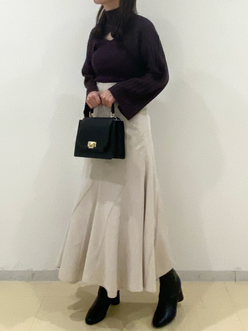 ブラウン系のニット/セーター、ベージュ系のスカート、ブラック系のハンドバッグを着用したレディースの秋コーディネートの2枚目の写真