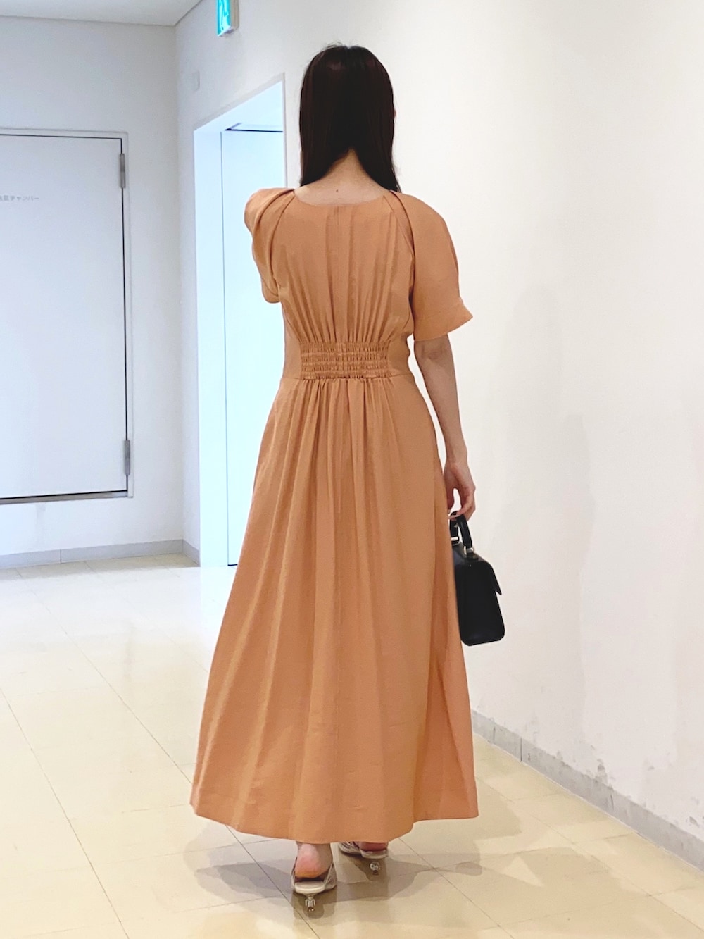 オレンジ系のワンピース、ブラック系のハンドバッグ、ホワイト系のサンダルを着用したレディースの春コーディネートの3枚目の写真