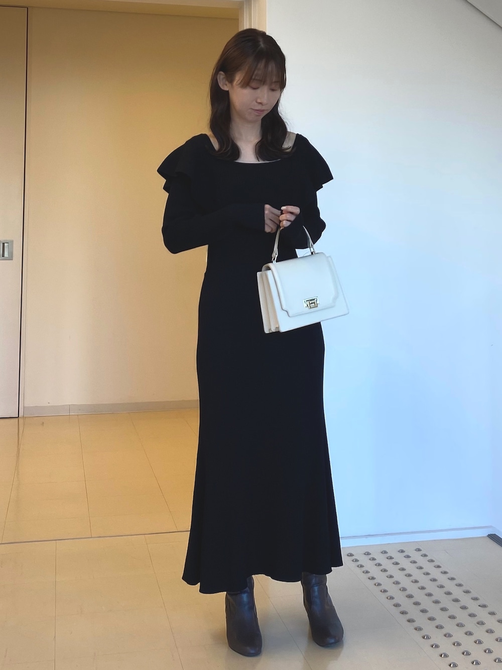 ブラック系のワンピース、ホワイト系のハンドバッグ、ブラウン系のブーツを着用したレディースの冬コーディネートの2枚目の写真