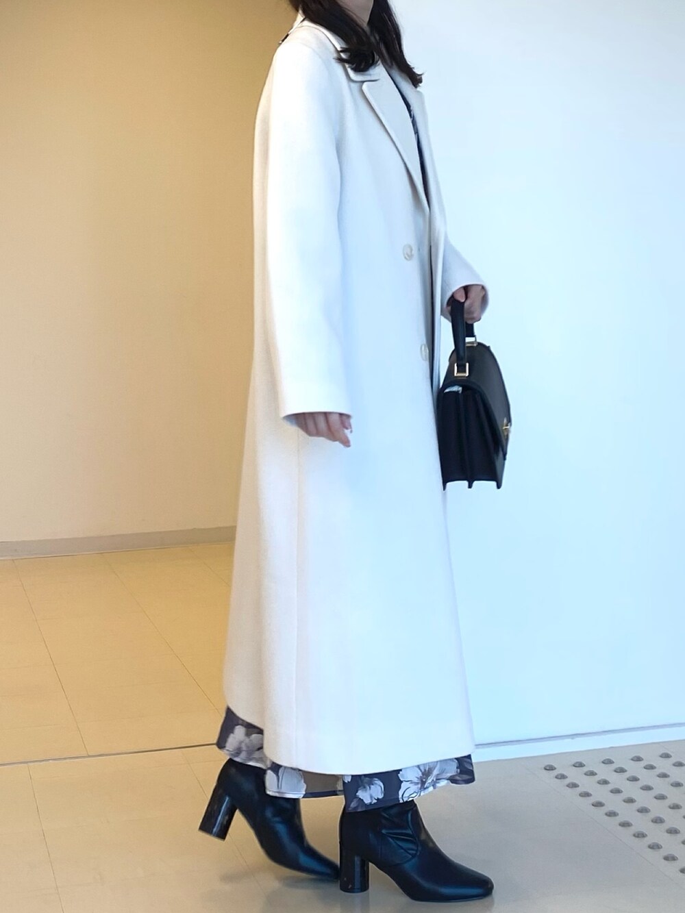 ホワイト系のチェスターコート、グレー系のワンピース、ブラック系のハンドバッグを着用したレディースの秋コーディネートの2枚目の写真