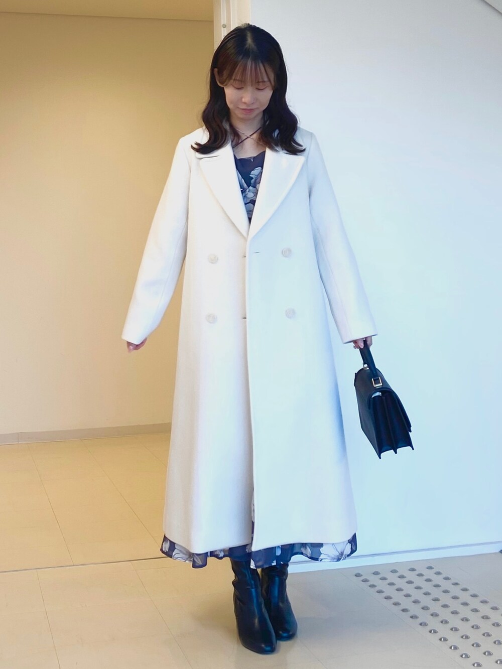 ホワイト系のチェスターコート、グレー系のワンピース、ブラック系のハンドバッグを着用したレディースの秋コーディネートの3枚目の写真