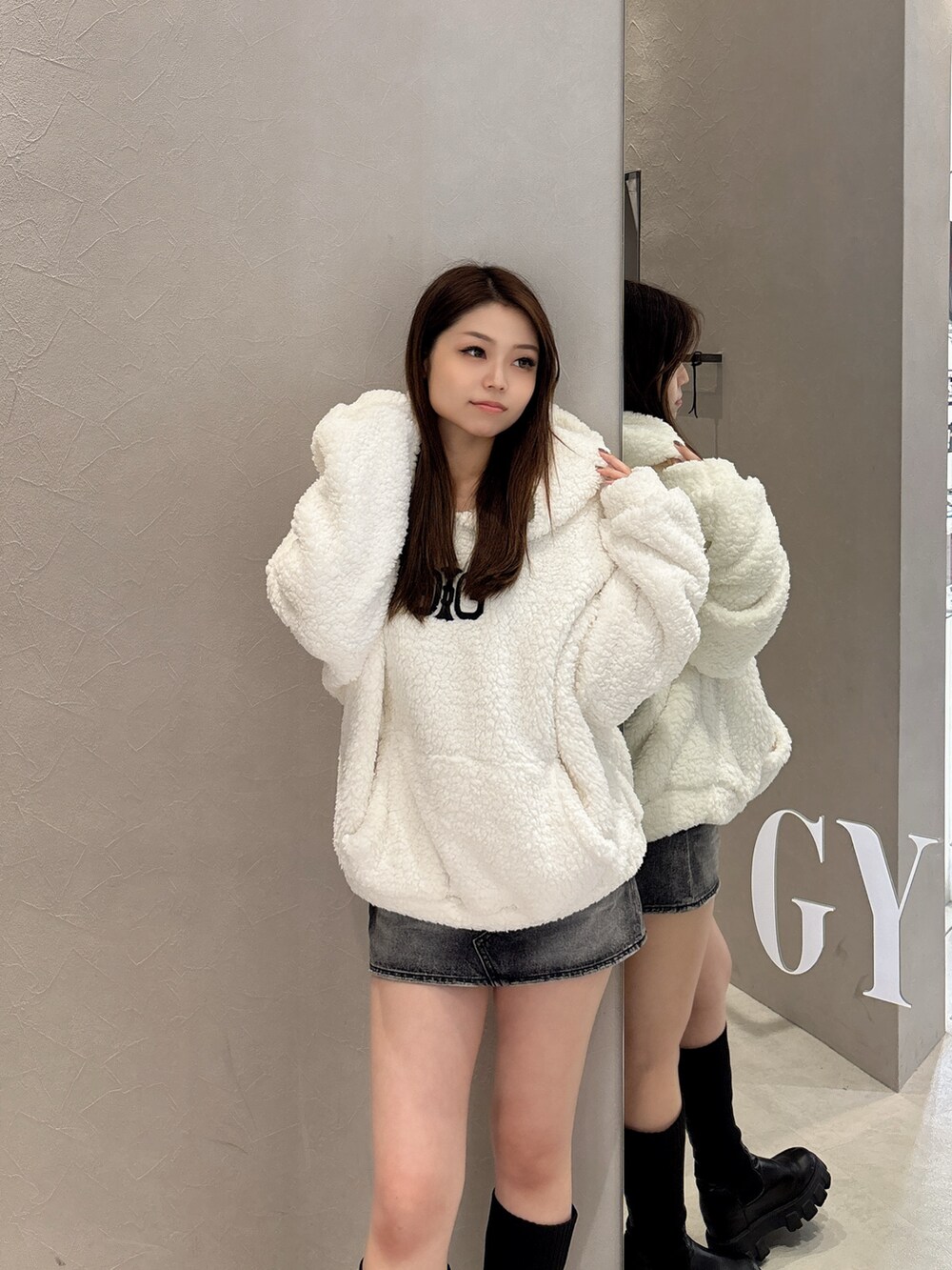 ホワイト系のパーカー、ブルー系のデニムスカート、ブラック系のブーツを着用したレディースの秋コーディネートの4枚目の写真