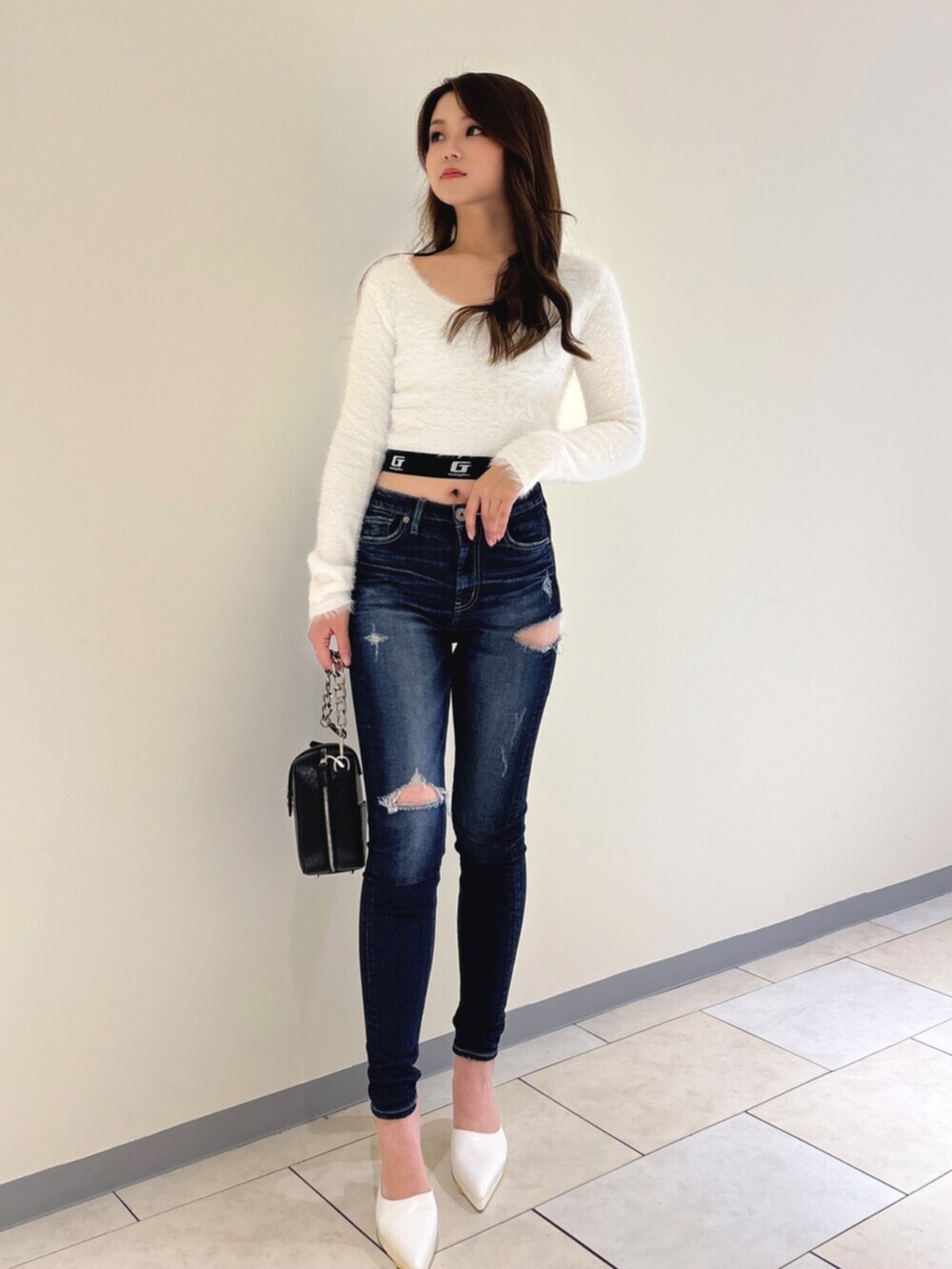 ホワイト系のパンプス、ブルー系のデニムパンツ、ブラック系のショルダーバッグを着用したレディースの冬コーディネートの2枚目の写真