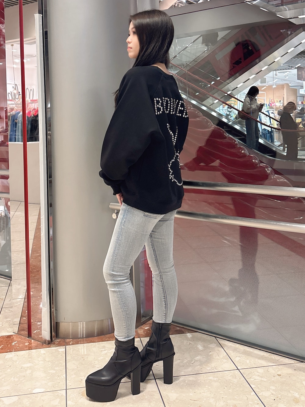 ブラック系のスウェット、ブルー系のデニムパンツ、ブラック系のブーツを着用したレディースの冬コーディネートの2枚目の写真