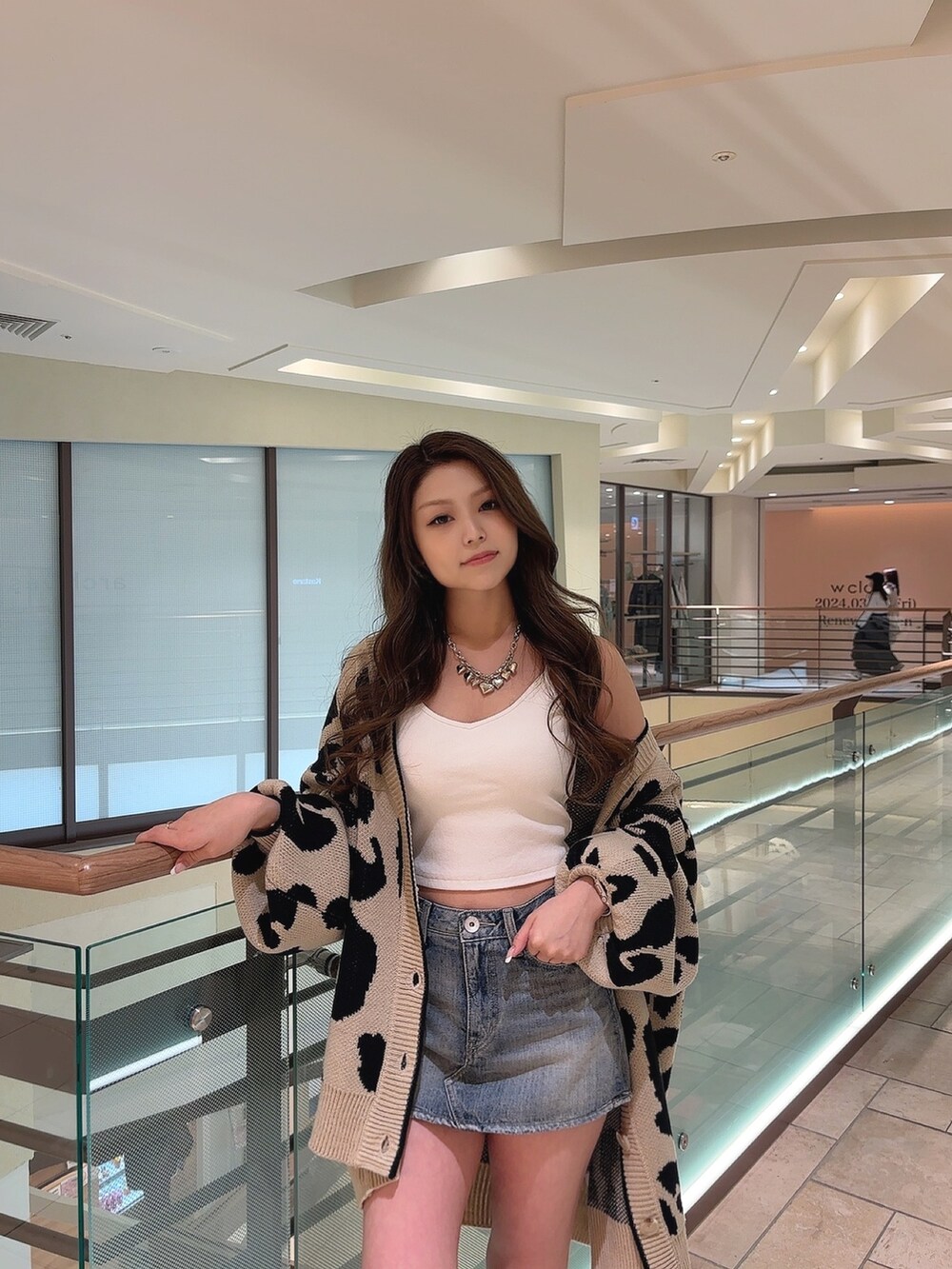 ベージュ系のカーディガン/ボレロ、ホワイト系のキャミソール、ブルー系のデニムスカートを着用したレディースの春コーディネートの5枚目の写真