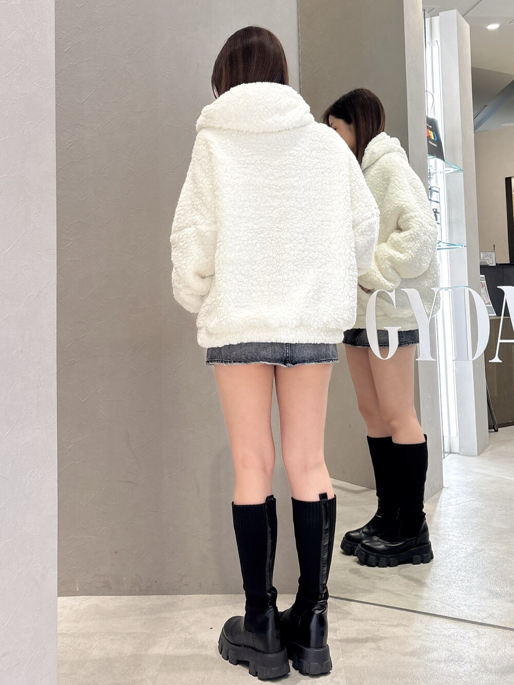 ホワイト系のパーカー、ブルー系のデニムスカート、ブラック系のブーツを着用したレディースの秋コーディネートの3枚目の写真