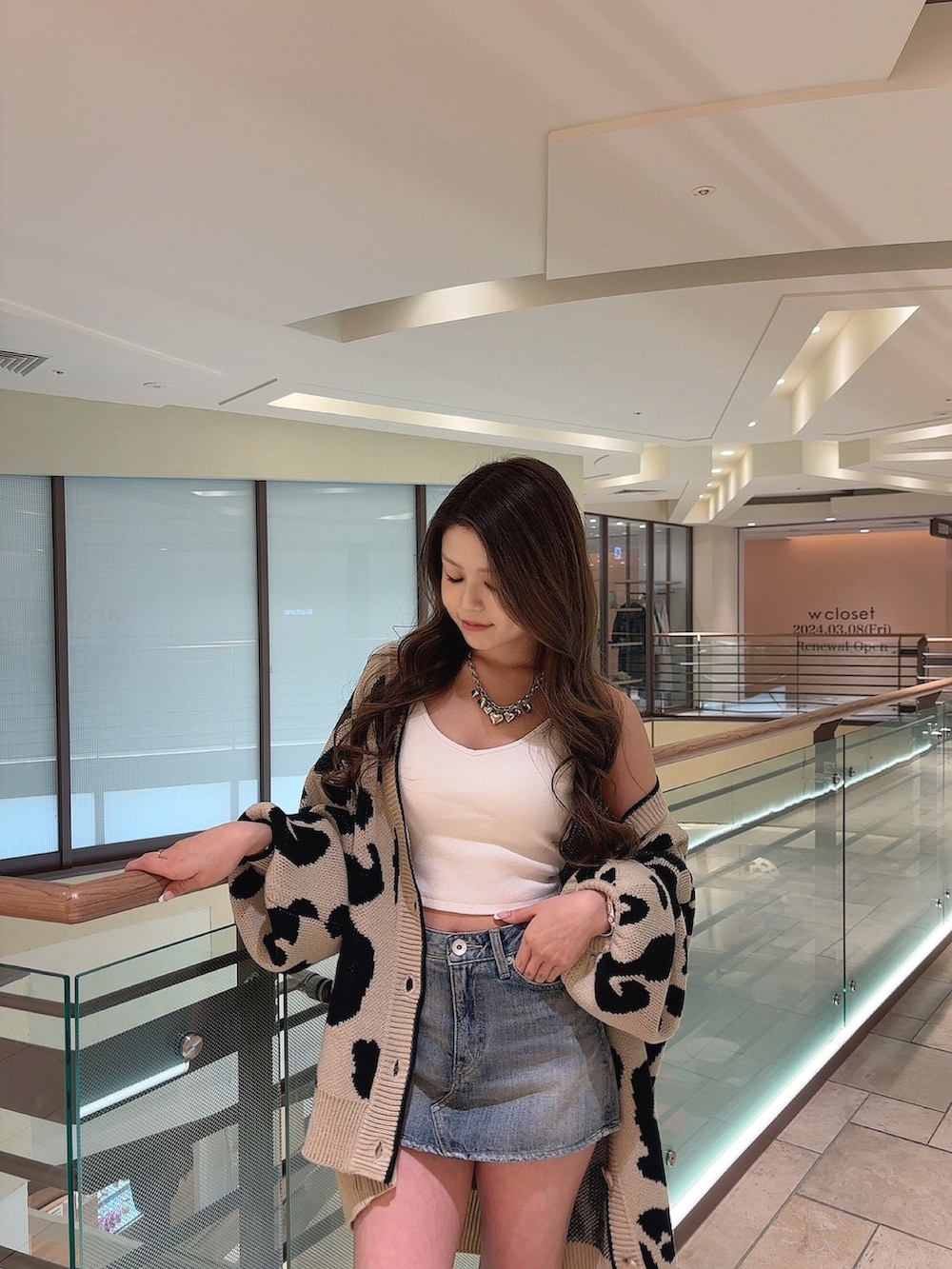 ベージュ系のカーディガン/ボレロ、ホワイト系のキャミソール、ブルー系のデニムスカートを着用したレディースの春コーディネートの6枚目の写真