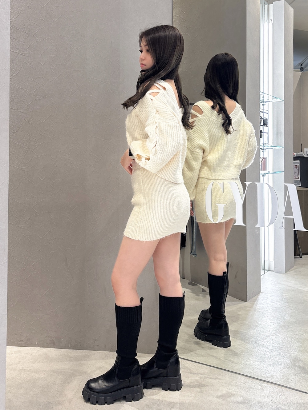 ホワイト系のニット/セーター、ホワイト系のスカート、ブラック系のブーツを着用したレディースの秋コーディネートの2枚目の写真