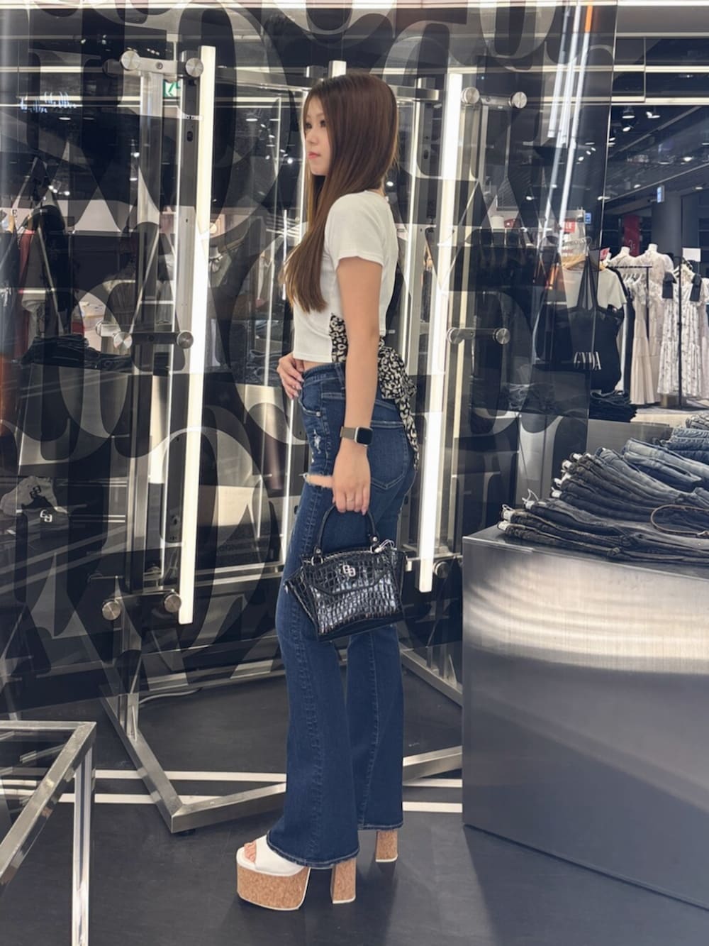 ホワイト系のサンダル、ホワイト系のハンドバッグ、ブルー系のデニムパンツを着用したレディースの夏コーディネートの2枚目の写真