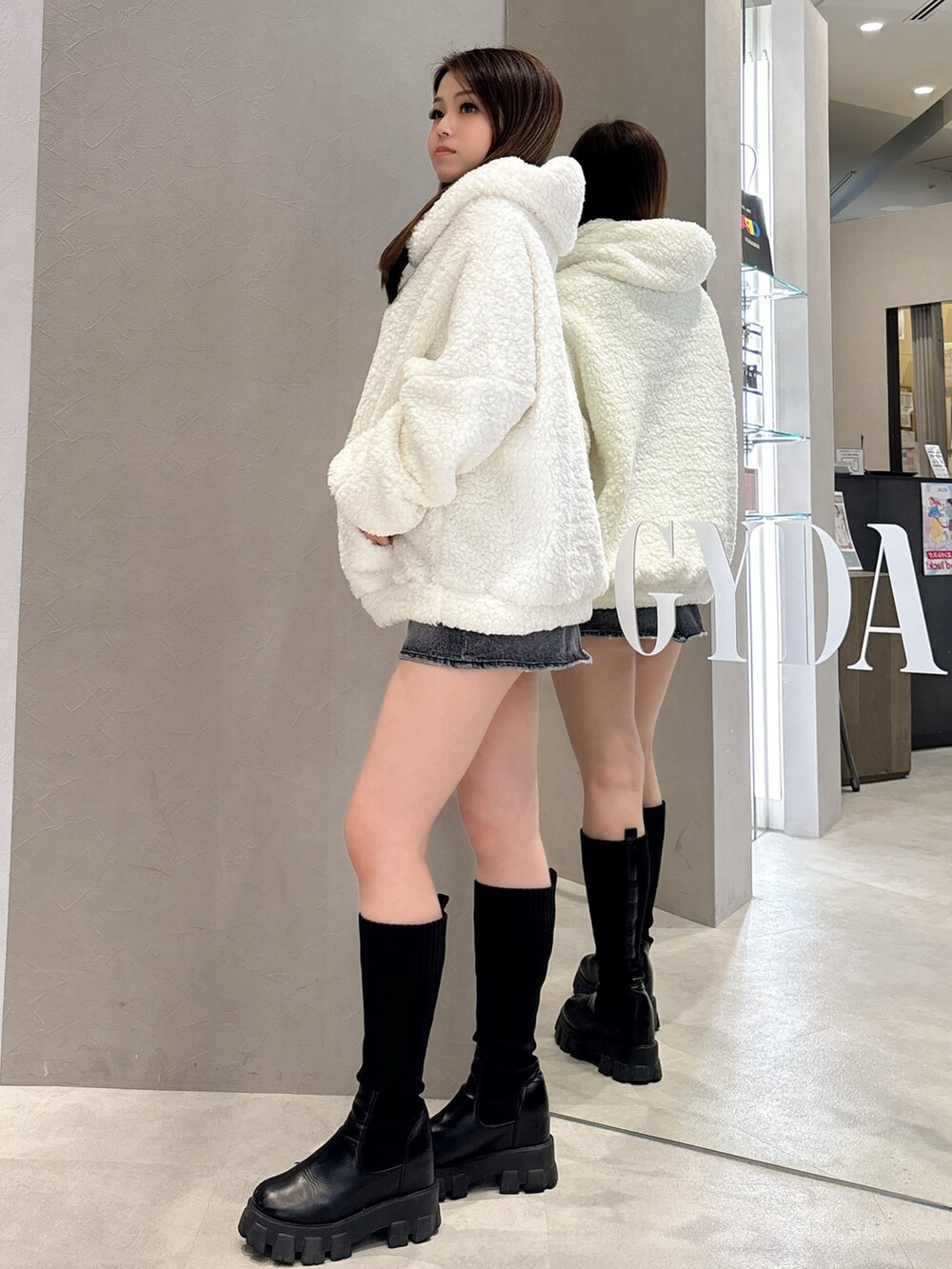 ホワイト系のパーカー、ブルー系のデニムスカート、ブラック系のブーツを着用したレディースの秋コーディネートの2枚目の写真