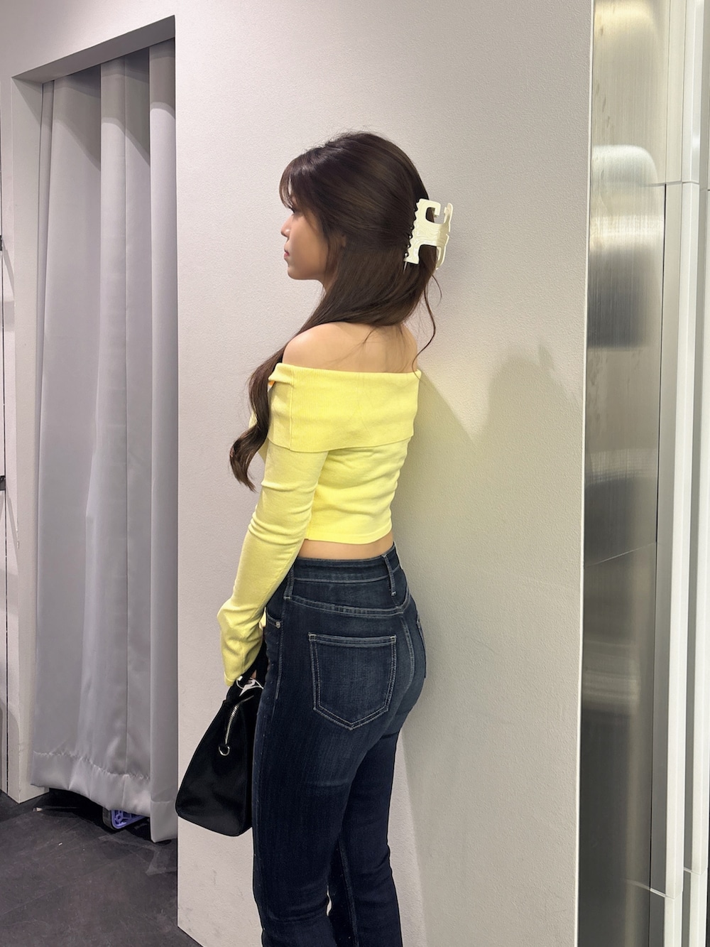 イエロー系のニット/セーター、ブラック系のハンドバッグ、ブルー系のデニムパンツを着用したレディースの秋コーディネートの5枚目の写真