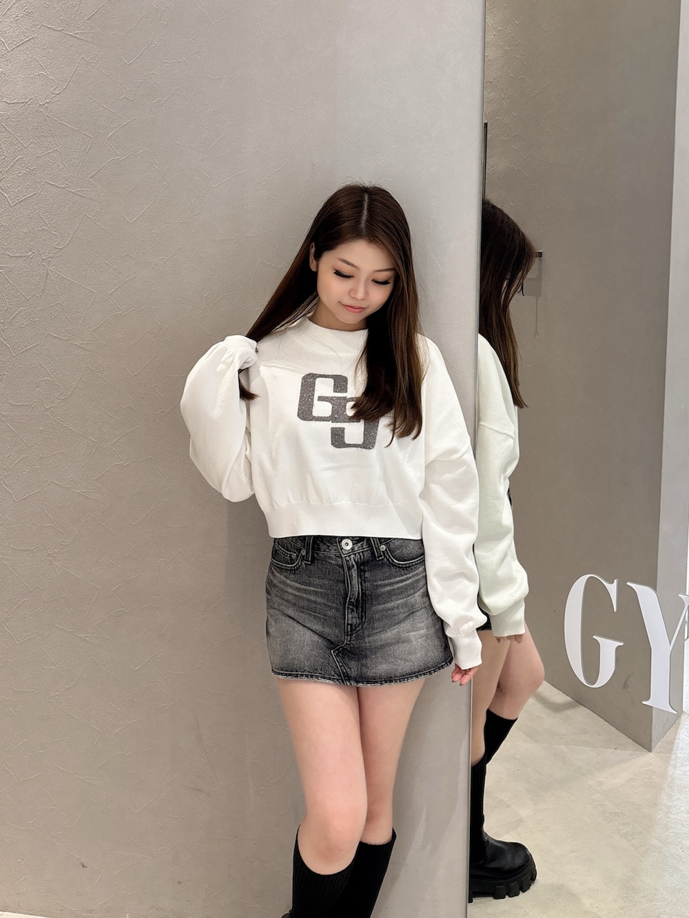 ホワイト系のニット/セーター、ブルー系のデニムスカート、ブラック系のブーツを着用したレディースの秋コーディネートの4枚目の写真