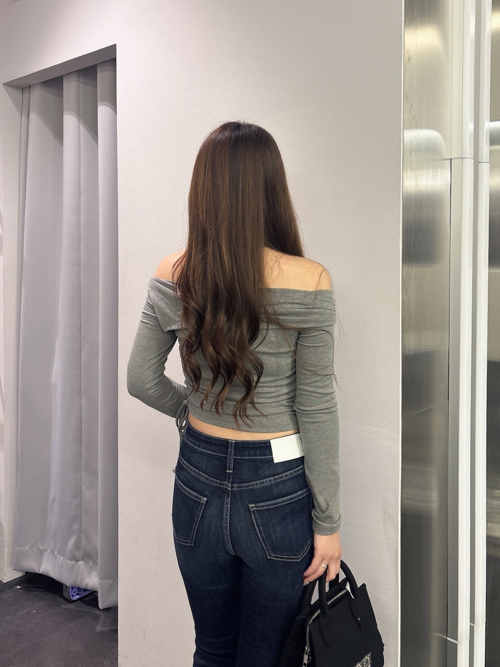 グレー系のTシャツ/カットソー、ブルー系のデニムパンツ、ブラック系のハンドバッグを着用したレディースの秋コーディネートの6枚目の写真