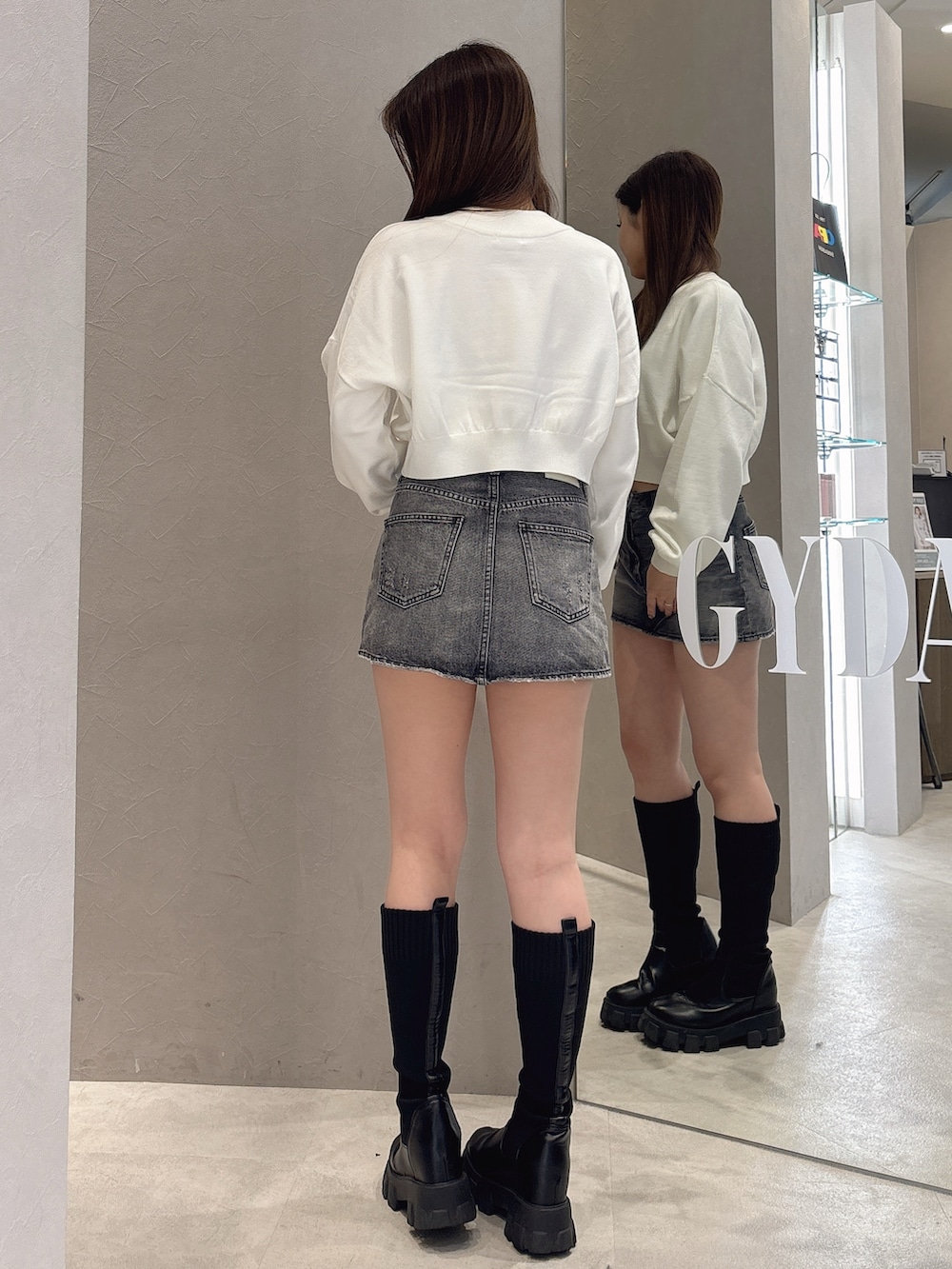 ホワイト系のニット/セーター、ブルー系のデニムスカート、ブラック系のブーツを着用したレディースの秋コーディネートの3枚目の写真