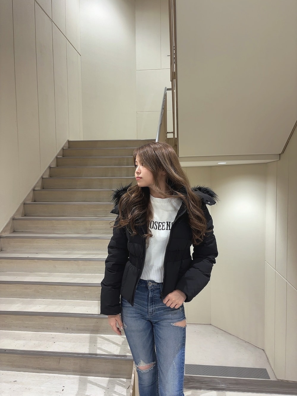 ブラック系のダウンジャケット/コート、ホワイト系のニット/セーター、ブルー系のデニムパンツを着用したレディースの秋コーディネートの5枚目の写真