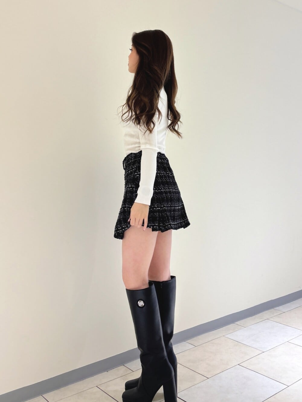 ブラック系のブーツ、ブラック系のスカート、ホワイト系のニット/セーターを着用したレディースの冬コーディネートの2枚目の写真