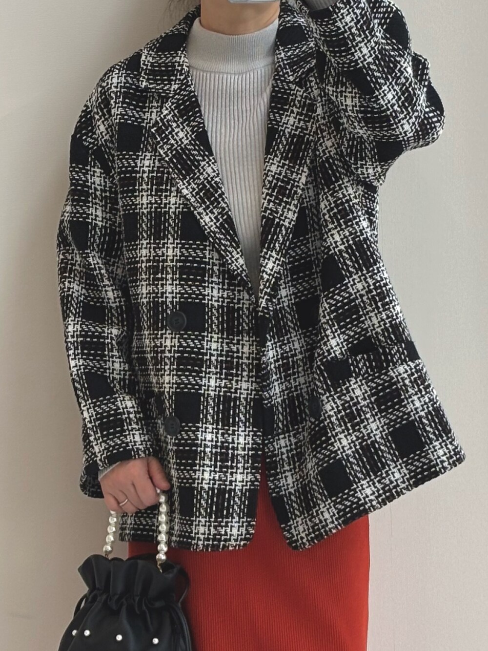 グレー系のニット/セーター、オレンジ系のスカート、ブラック系のジャケット/アウターを着用したレディースの秋コーディネートの3枚目の写真