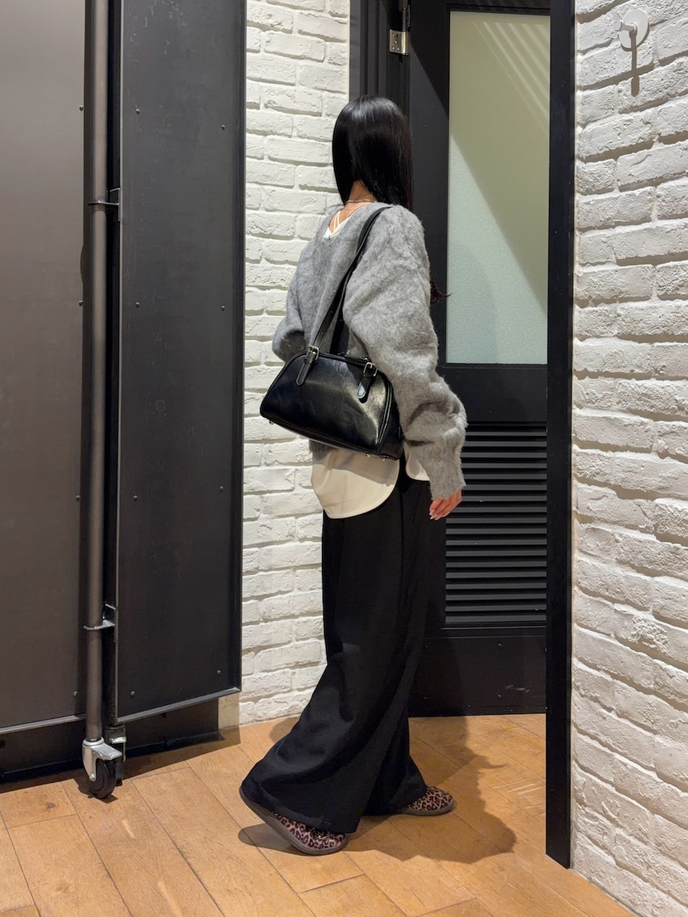 ブラック系のスラックス、ホワイト系のTシャツ/カットソー、グレー系のニット/セーターを着用したレディースの冬コーディネートの2枚目の写真