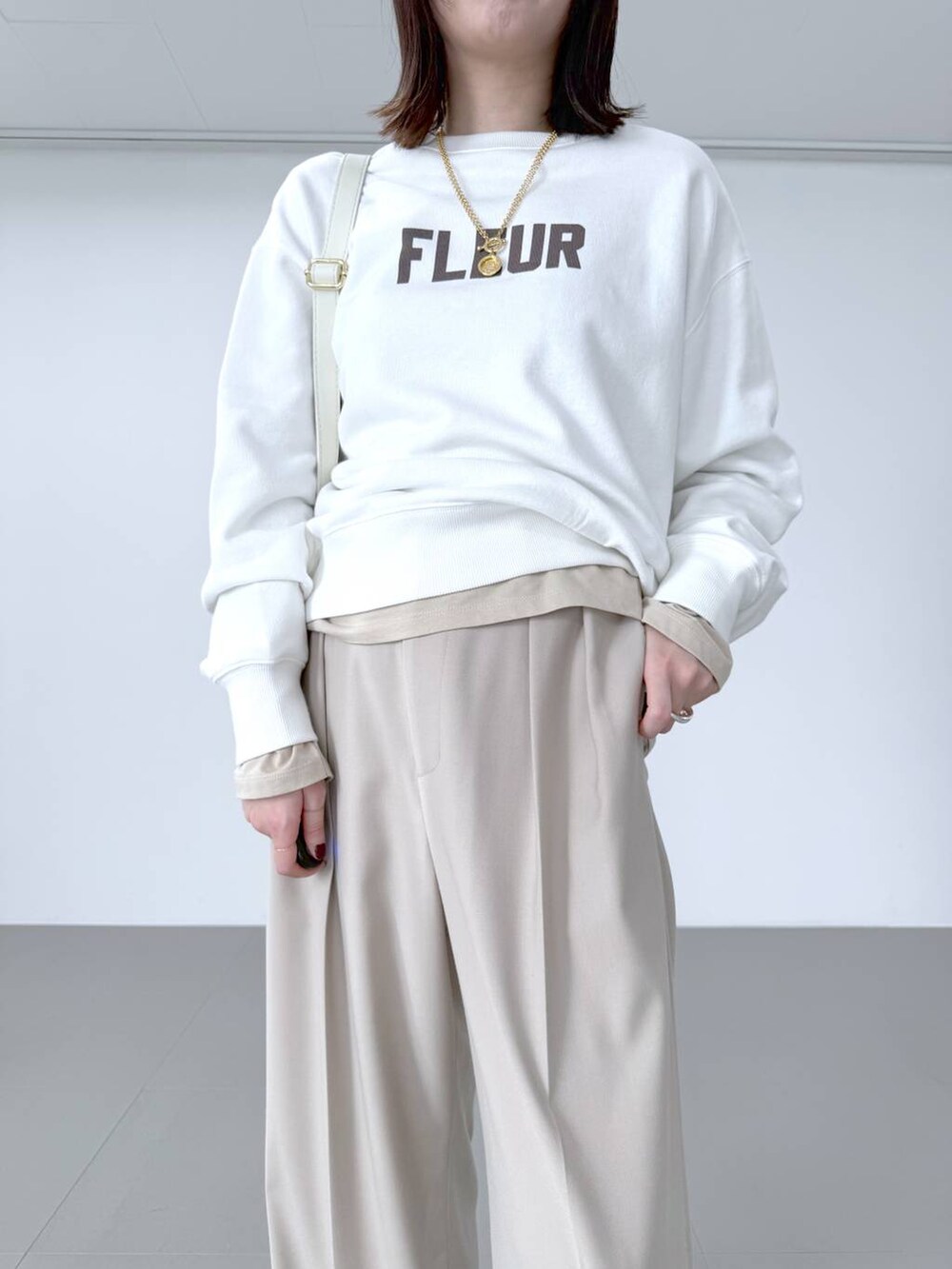 ホワイト系のスウェット、ホワイト系のショルダーバッグ、ベージュ系のスラックスを着用したレディースの冬コーディネートの3枚目の写真