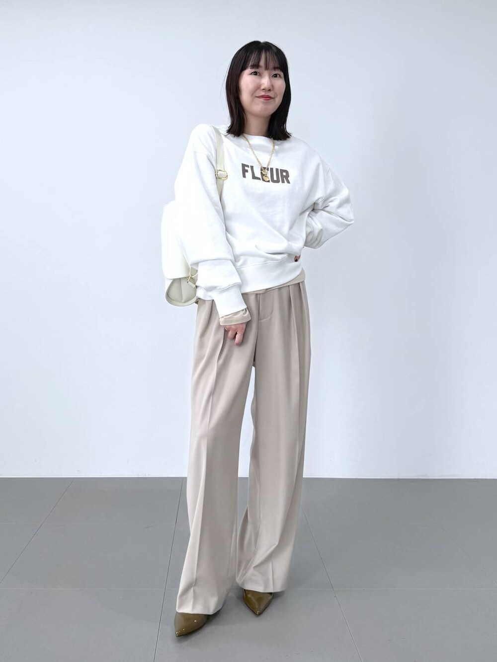 ホワイト系のスウェット、ホワイト系のショルダーバッグ、ベージュ系のスラックスを着用したレディースの冬コーディネートの2枚目の写真