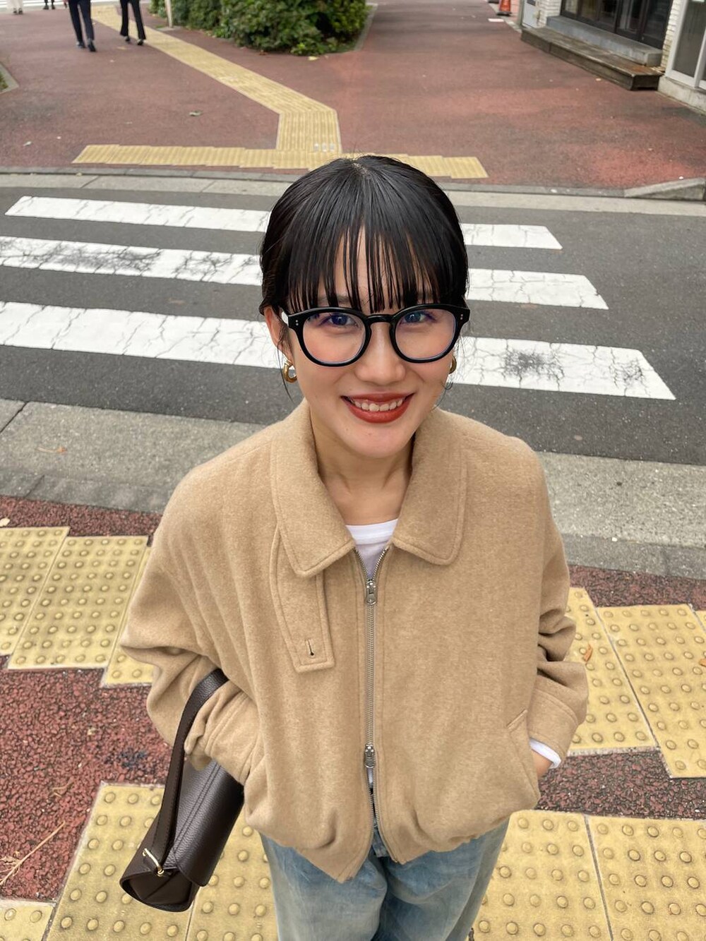 ブラウン系のショルダーバッグ、ブルー系のデニムパンツ、ベージュ系のブルゾンを着用したレディースの冬コーディネートの2枚目の写真